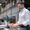 Mann arbeitet mit Laptop in einer industriellen Produktionshalle